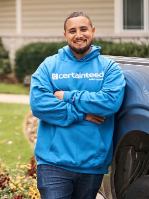 A man in a blue CertainTeed hoodie leaning on a truck